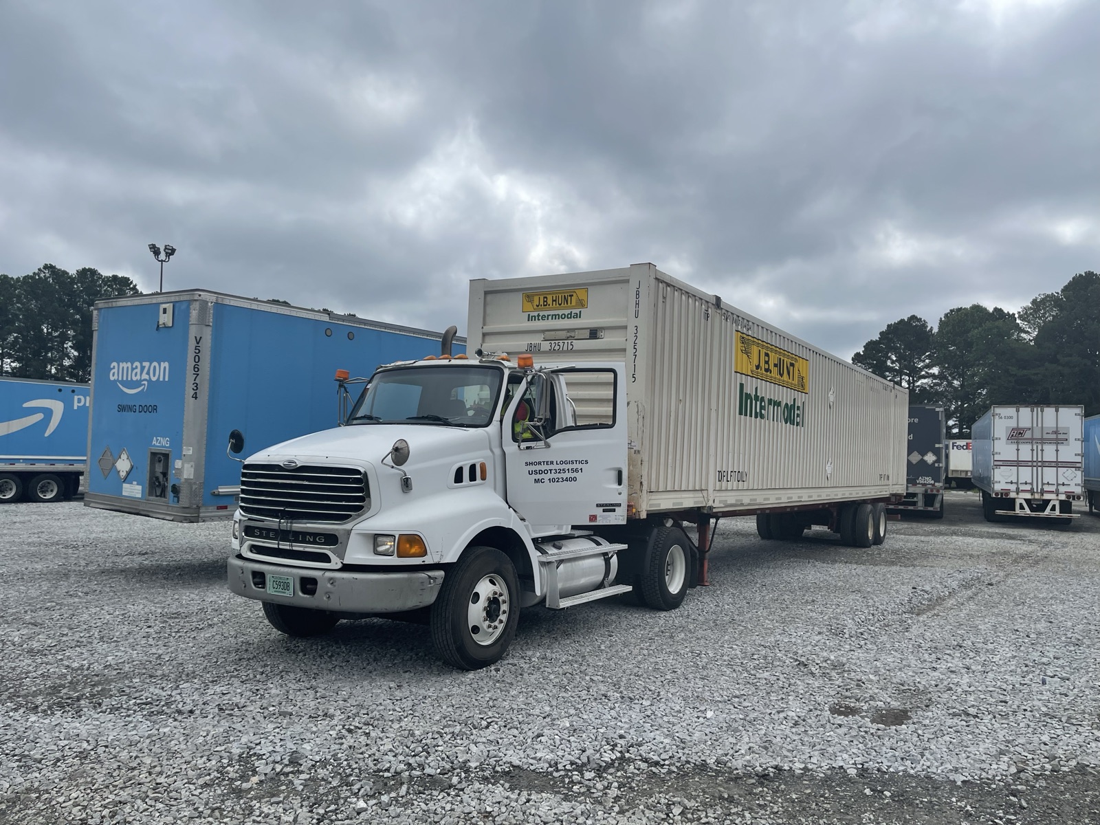 A white Shorter Logistics day cab hooked to an intermodal container on a chassis in a gravel trailer yard.